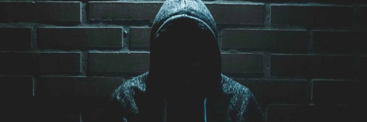 Un voleur au visage caché devant un mur en brique