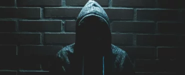 Un voleur au visage caché devant un mur en brique